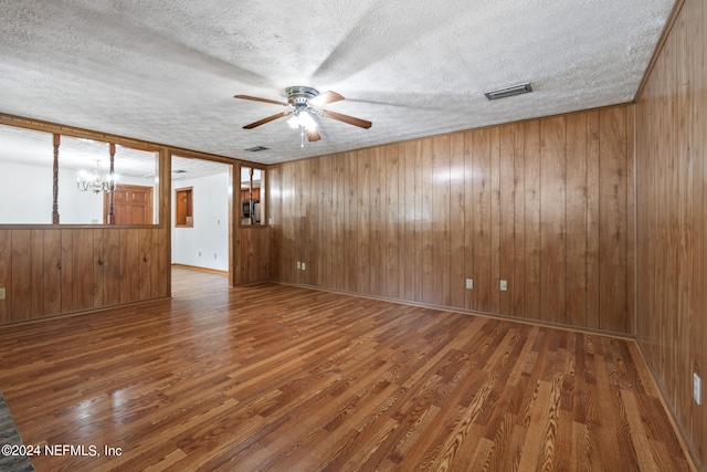 unfurnished room featuring ceiling fan with notable chandelier, wooden walls, a textured ceiling, and dark hardwood / wood-style flooring