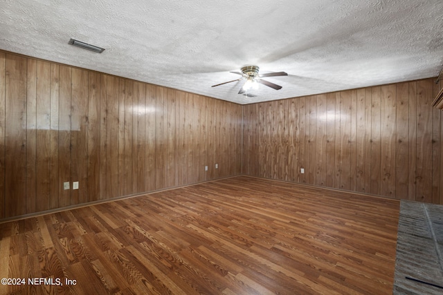 unfurnished room featuring ceiling fan, a textured ceiling, wood walls, and dark hardwood / wood-style floors