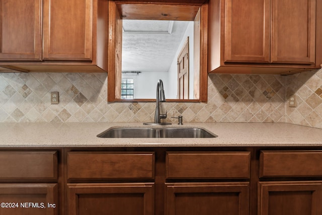 kitchen featuring backsplash, a textured ceiling, sink, and light stone countertops