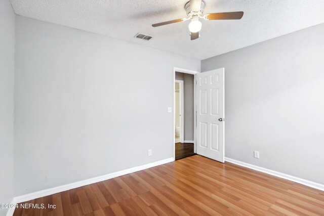 empty room with a textured ceiling, ceiling fan, wood finished floors, visible vents, and baseboards