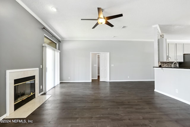 unfurnished living room featuring dark wood-style flooring, a fireplace, a ceiling fan, baseboards, and ornamental molding