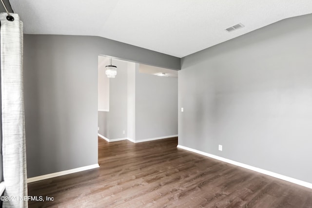 empty room with lofted ceiling, wood finished floors, visible vents, and baseboards