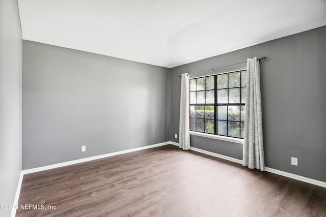 empty room with a textured ceiling, baseboards, and wood finished floors