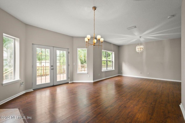 spare room featuring a textured ceiling, dark wood-type flooring, a notable chandelier, and french doors