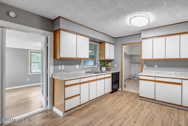 kitchen with white cabinets, a textured ceiling, light hardwood / wood-style flooring, and sink