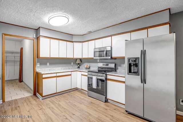 kitchen with appliances with stainless steel finishes, white cabinets, a textured ceiling, and light wood-type flooring