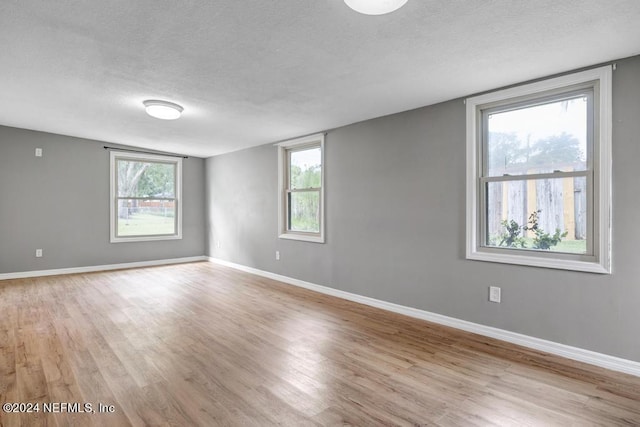 empty room with a textured ceiling, light hardwood / wood-style floors, and a healthy amount of sunlight