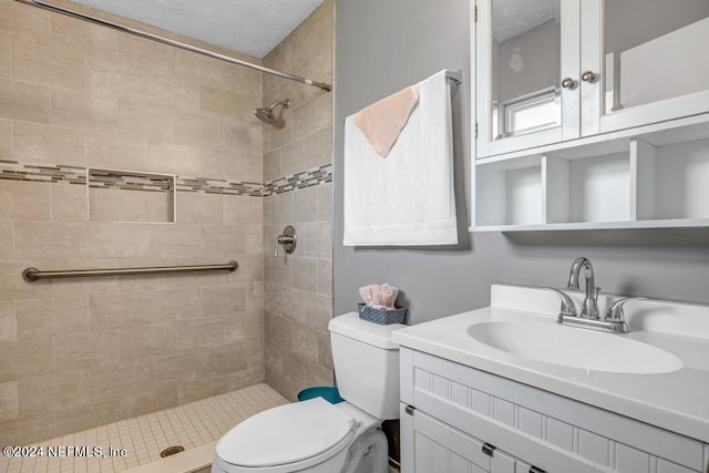 bathroom with toilet, a tile shower, and vanity