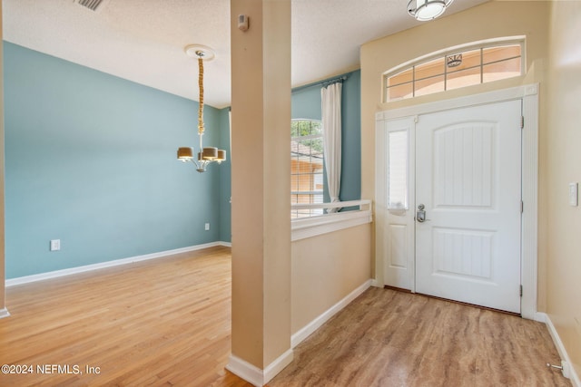 entrance foyer featuring a textured ceiling, light hardwood / wood-style flooring, and an inviting chandelier