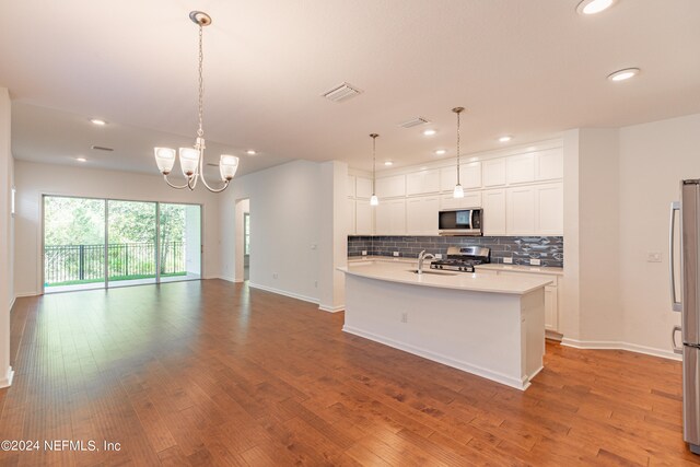 kitchen with decorative light fixtures, backsplash, appliances with stainless steel finishes, a kitchen island with sink, and light hardwood / wood-style floors