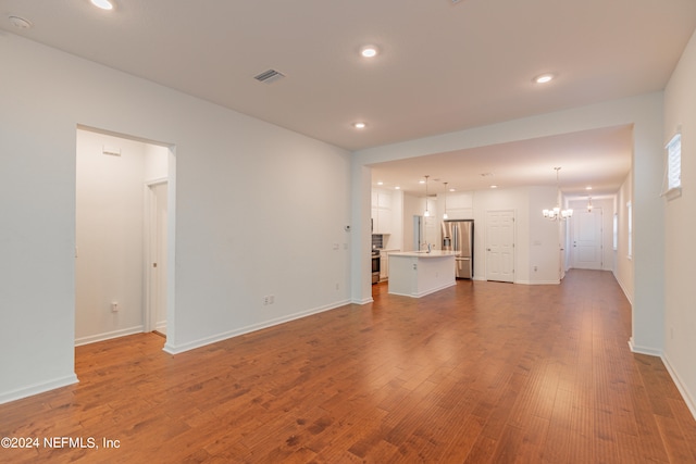 unfurnished living room with wood-type flooring and an inviting chandelier