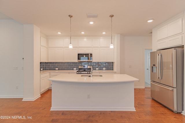 kitchen with white cabinetry, stainless steel appliances, decorative backsplash, a center island with sink, and light hardwood / wood-style floors