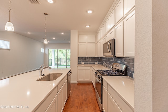 kitchen with appliances with stainless steel finishes, sink, dark wood-type flooring, pendant lighting, and decorative backsplash