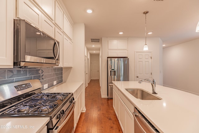 kitchen featuring decorative light fixtures, wood-type flooring, appliances with stainless steel finishes, tasteful backsplash, and sink