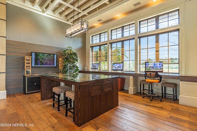 interior space with a kitchen bar, hanging light fixtures, wood-type flooring, and beam ceiling