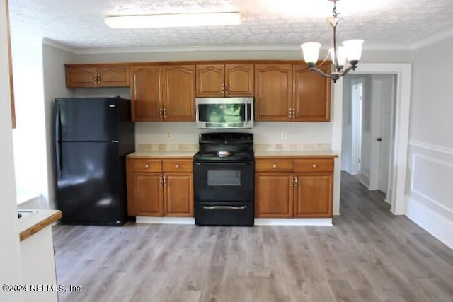 kitchen featuring hanging light fixtures, black appliances, a textured ceiling, crown molding, and light wood-type flooring