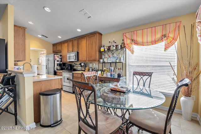 kitchen featuring sink, kitchen peninsula, lofted ceiling, light tile patterned floors, and appliances with stainless steel finishes