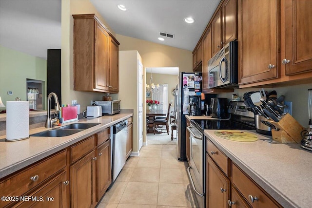 kitchen with appliances with stainless steel finishes, vaulted ceiling, sink, light tile patterned floors, and an inviting chandelier