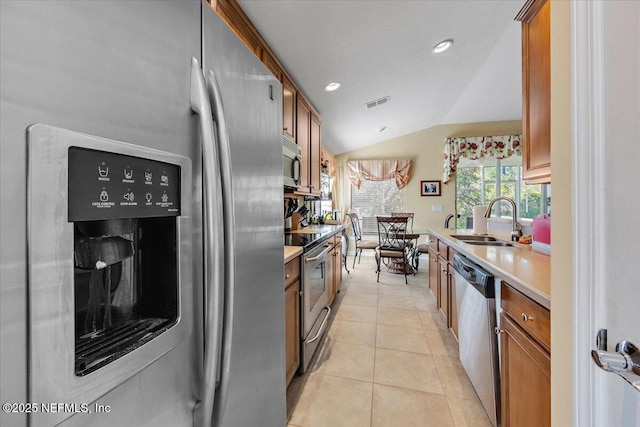 kitchen featuring sink, light tile patterned floors, vaulted ceiling, and appliances with stainless steel finishes