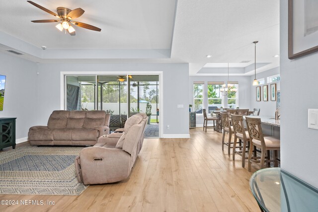 living room with ceiling fan, a raised ceiling, and light hardwood / wood-style floors