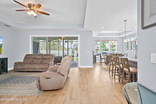 living room featuring light wood-style floors, visible vents, a tray ceiling, and baseboards