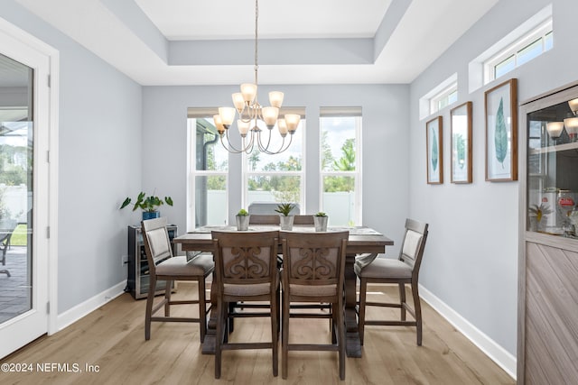 dining area featuring light wood finished floors, baseboards, a tray ceiling, and a chandelier