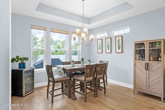 dining room featuring light wood-type flooring, a raised ceiling, a chandelier, and a healthy amount of sunlight