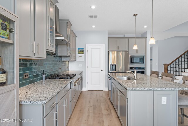 kitchen featuring light hardwood / wood-style flooring, appliances with stainless steel finishes, an island with sink, hanging light fixtures, and a breakfast bar