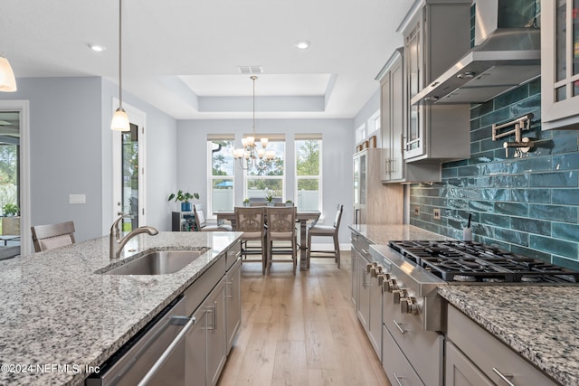 kitchen featuring appliances with stainless steel finishes, a raised ceiling, hanging light fixtures, and wall chimney range hood