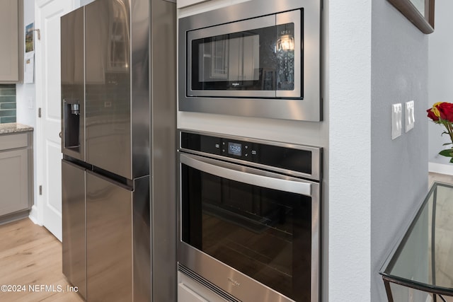 kitchen with light wood finished floors, appliances with stainless steel finishes, and light stone countertops