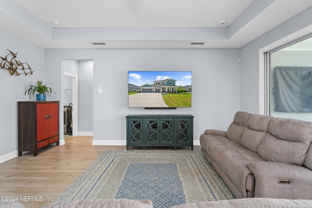 living room with a healthy amount of sunlight, a tray ceiling, and hardwood / wood-style flooring