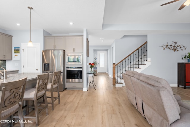 kitchen with light stone counters, a breakfast bar area, light wood-style flooring, stainless steel appliances, and gray cabinets