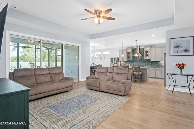 living room with light wood-type flooring and ceiling fan with notable chandelier