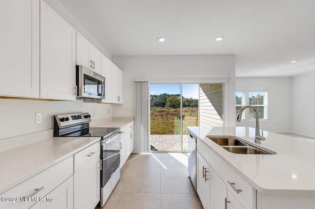 kitchen with sink, stainless steel appliances, light tile patterned floors, a kitchen island with sink, and white cabinets