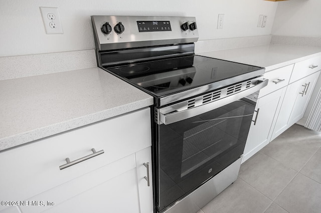 kitchen with white cabinets, light tile patterned floors, and electric range