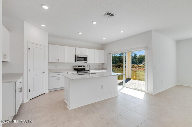 kitchen featuring a kitchen island with sink, white cabinets, sink, light tile patterned floors, and stainless steel appliances