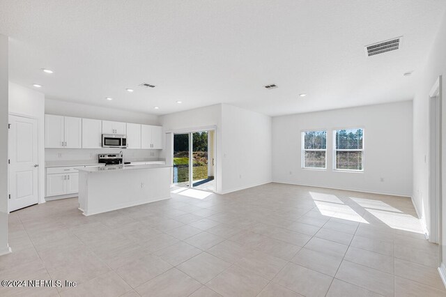 kitchen featuring a kitchen island with sink, white cabinets, light tile patterned flooring, and appliances with stainless steel finishes