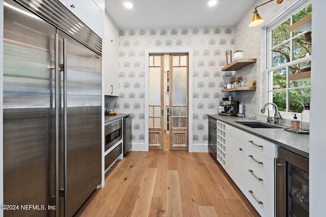 kitchen with light wood-type flooring, beverage cooler, built in refrigerator, white cabinets, and sink