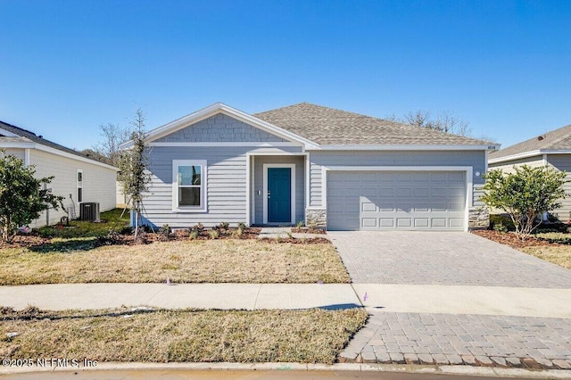 view of front of home featuring decorative driveway, a garage, stone siding, and roof with shingles