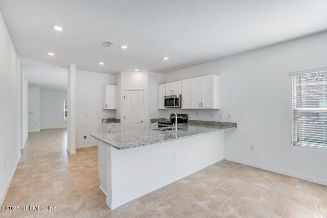 kitchen with light stone counters, visible vents, a peninsula, a sink, and stainless steel microwave