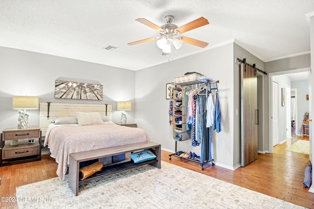 bedroom featuring light hardwood / wood-style floors, a textured ceiling, a barn door, a closet, and ceiling fan