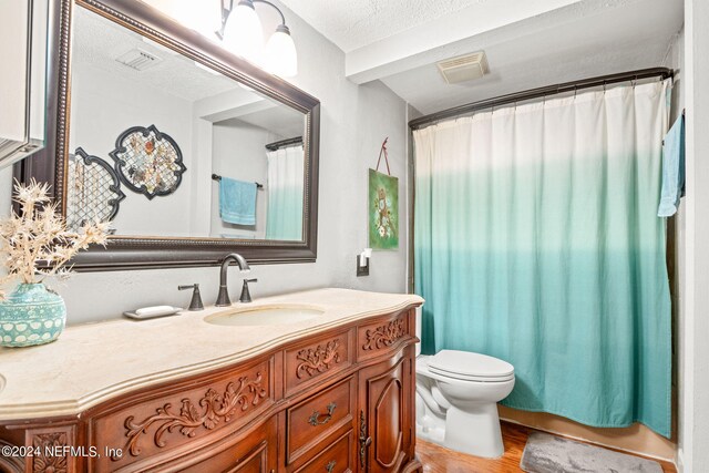 bathroom featuring wood-type flooring, a textured ceiling, a shower with shower curtain, vanity, and toilet