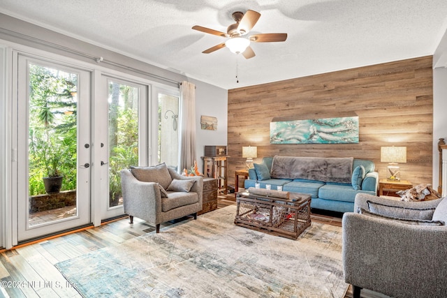 living room with wood walls, french doors, a textured ceiling, wood-type flooring, and ceiling fan