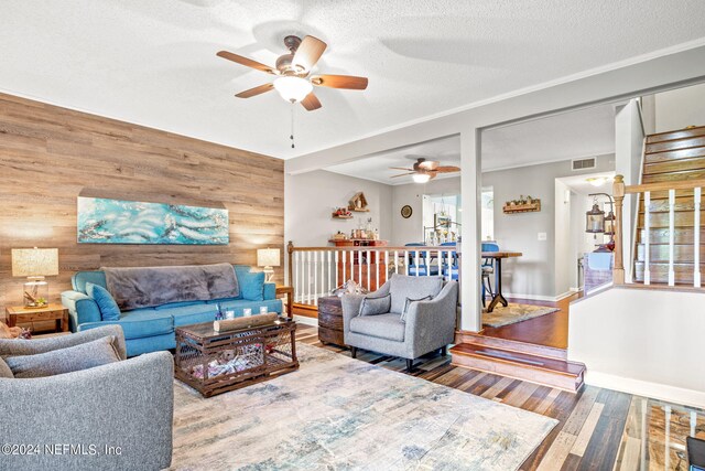 living room featuring a textured ceiling, ceiling fan, wood walls, and wood-type flooring