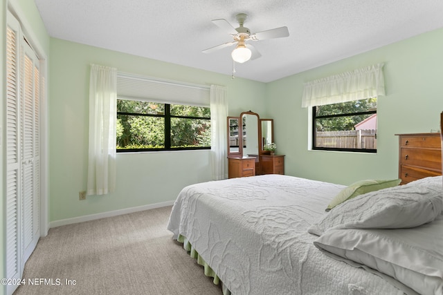 bedroom featuring light carpet, multiple windows, ceiling fan, and a closet