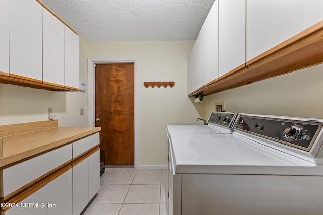 washroom with light tile patterned floors, a textured ceiling, cabinets, and washer and clothes dryer