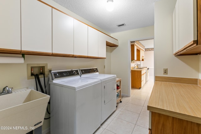 clothes washing area featuring independent washer and dryer, sink, light tile patterned flooring, cabinets, and a textured ceiling