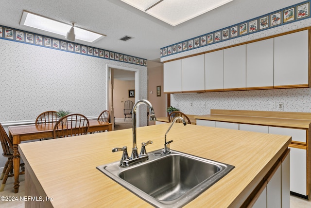 kitchen featuring a textured ceiling, sink, and white cabinets