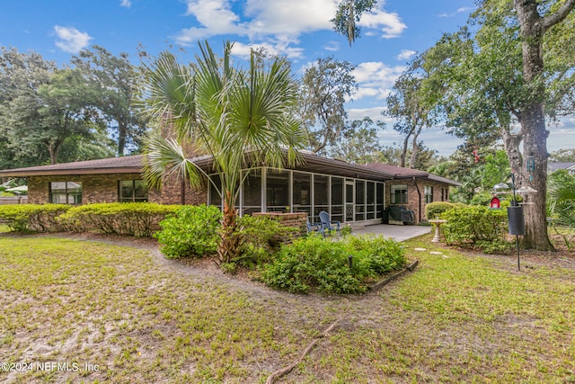 rear view of house featuring a lawn, a patio, and a sunroom