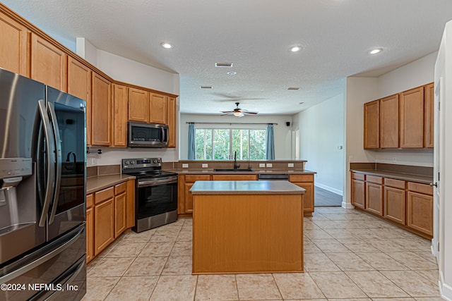 kitchen with stainless steel appliances, sink, ceiling fan, a kitchen island, and a textured ceiling